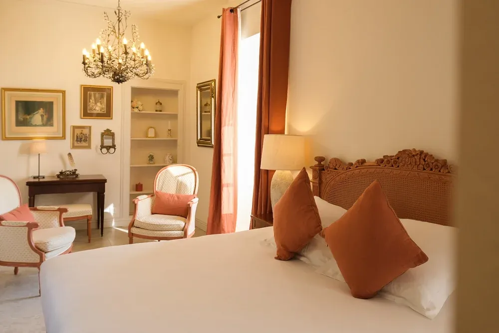Chambre lumineuse avec lustre, lit à tête de lit sculptée et coussins terracotta